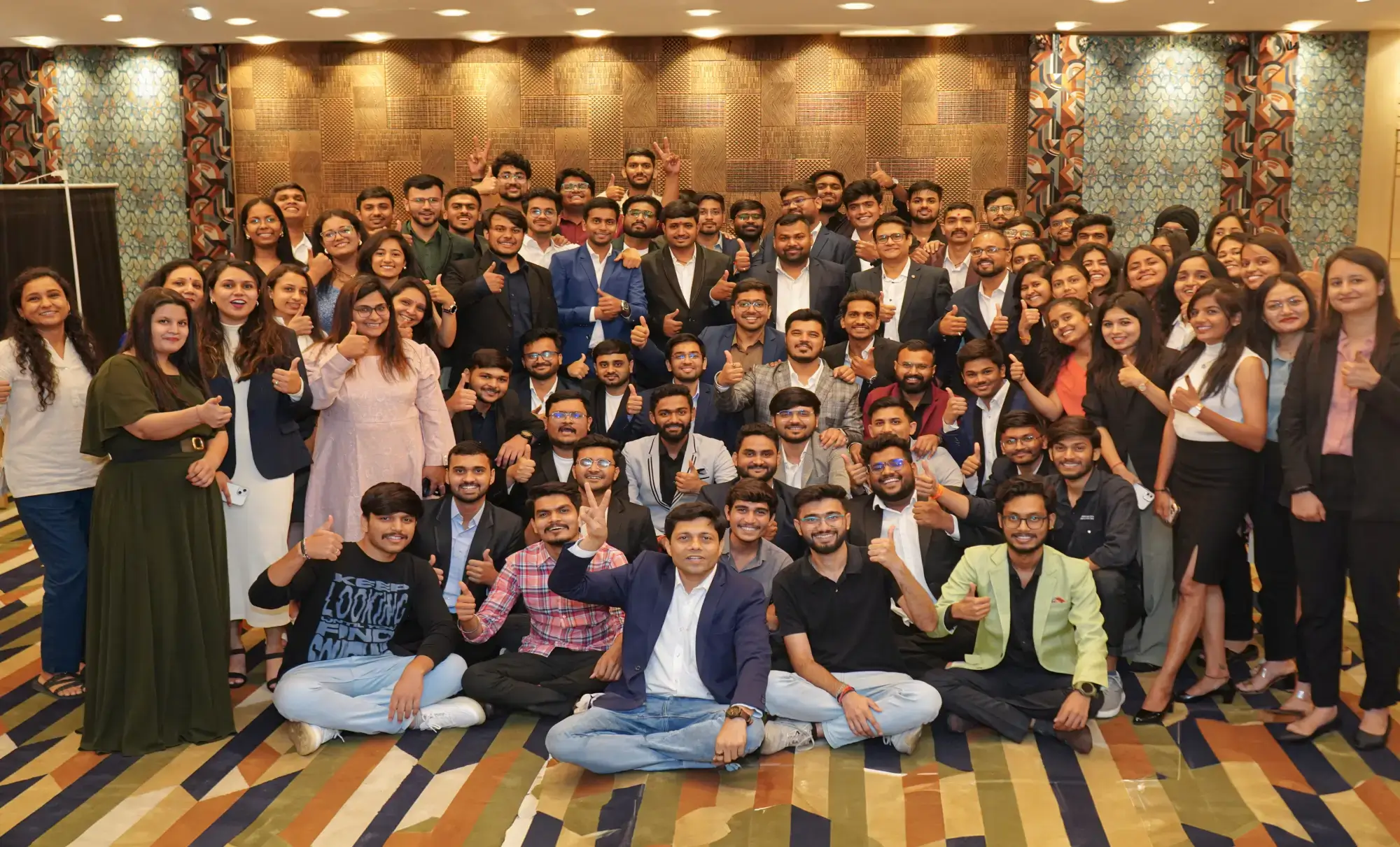 Large team of professionals posing together at corporate event with smiles and thumbs up in formal attire
