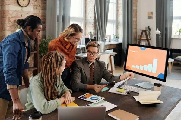 Diverse team reviewing charts and analytics during a business meeting, discussing growth strategy around a large office desk